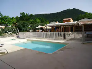 Schwimmbecken auf dem Campingplatz mit Sonnenschirmen, Liegen und Blick auf Bäume sowie Gebäude mit Terrassen.