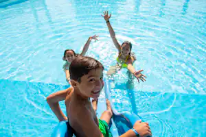 Kinder im Schwimmbecken, sie plantschen und halten sich am Beckenrand fest.