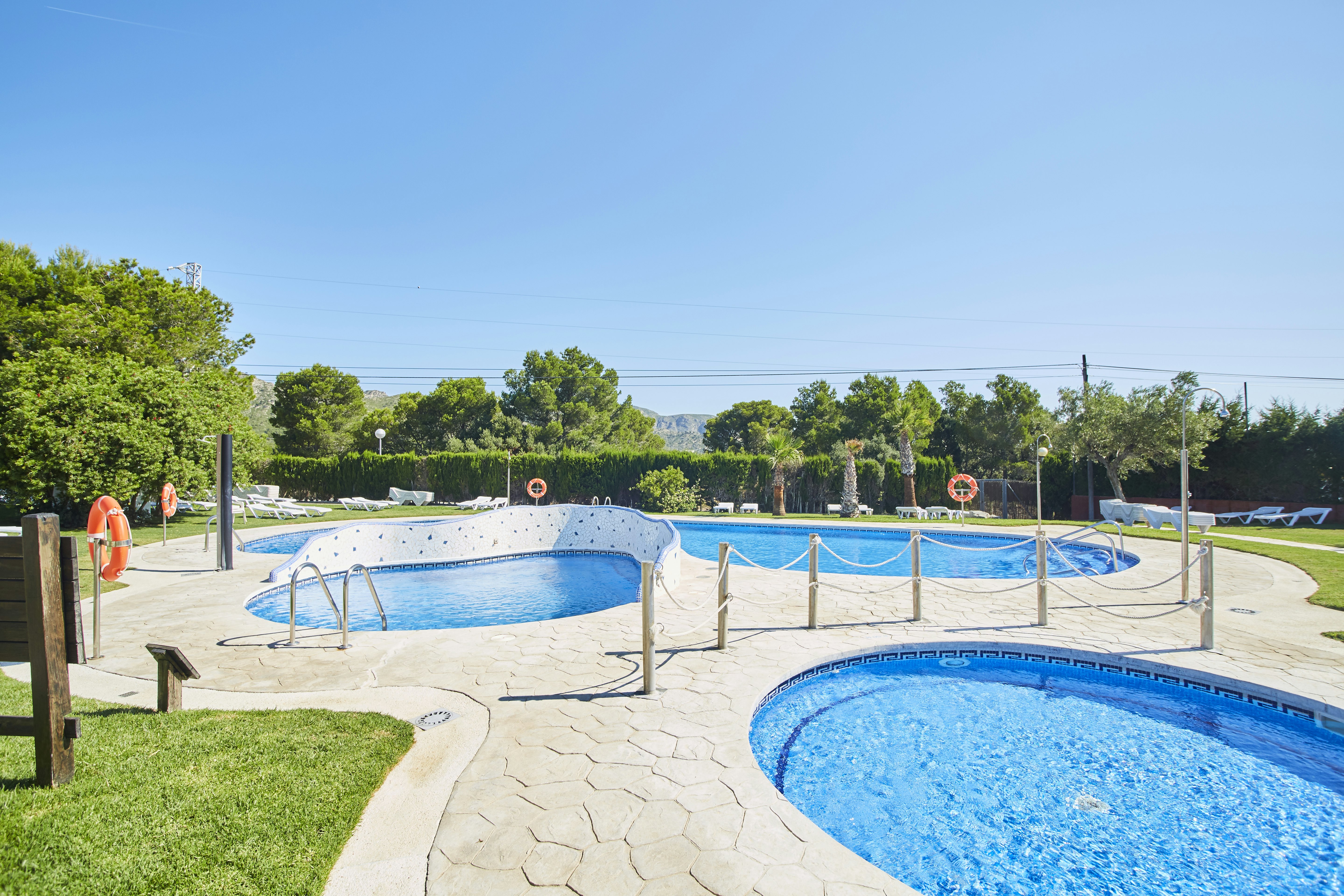 Zwei Camping-Schwimmbecken mit blauem Wasser, umzäunt mit Geländern, gepflasterter Bereich und Rasen am Rand.