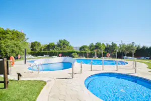 Zwei Camping-Schwimmbecken mit blauem Wasser, umzäunt mit Geländern, gepflasterter Bereich und Rasen am Rand.