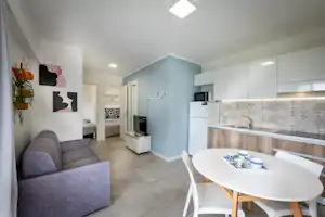 Modernes Wohnzimmer mit Sofa, Esstisch und Küchenzeile in einem hellen Wohnbereich mit Fliesenboden.