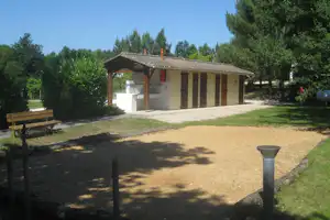 Campinghaus mit überdachter Terrasse, Grillbereich und Waschbecken, daneben ein Picknicktisch im Grünen.