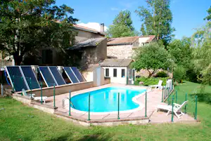 Schwimmbecken im Garten mit Liegen und Sonnenschirmen, dahinter Wohngebäude und Bäume am Campingplatz.