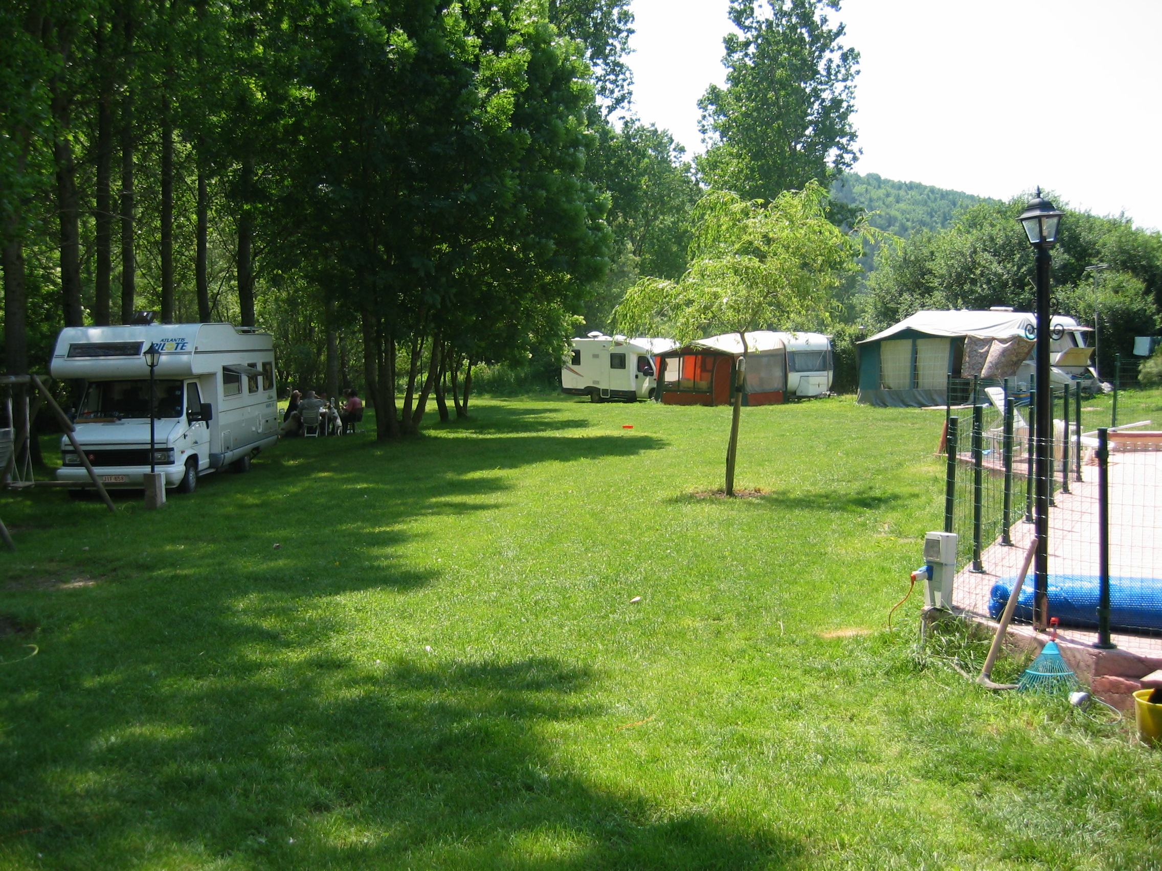 Campingwiese mit Wohnwagen und Zelten, Bäume am Rand und ein Weg zwischen den Stellplätzen.