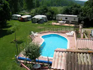 Privater Pool mit Liegen und Gartenzaun, daneben Wohnwagen und Zelte auf dem Campingplatz im Grünen.