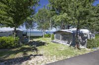 Camping La Perla del Lago - Wohnwagen zwischen Bäumen mit dem Bolsenasee im Hintergrund