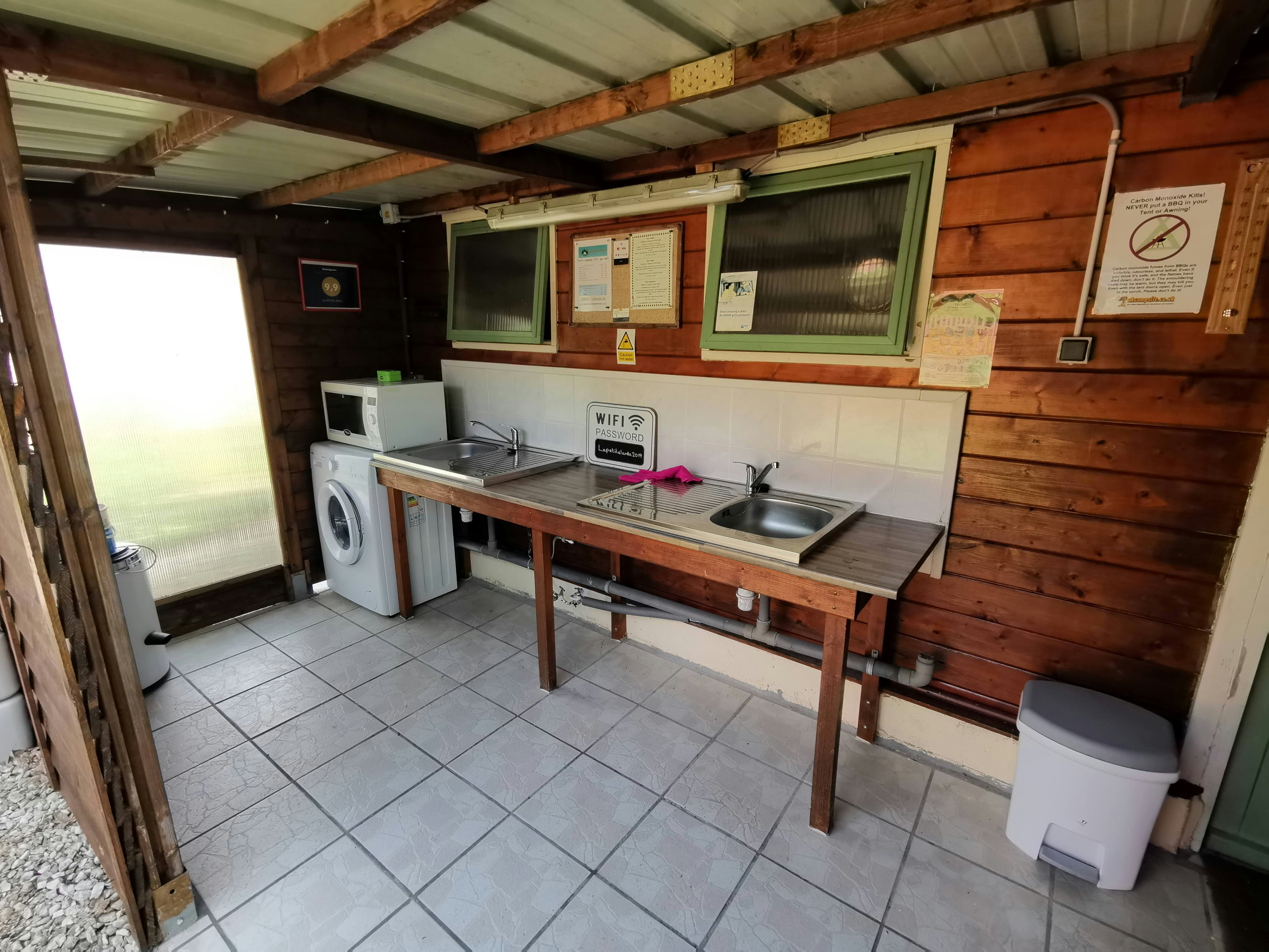 Holzhaus mit Küchenzeile: Spüle, Arbeitsplatte, Kühlschrank und Waschmaschine, Fliesenboden und Schrankwände an der Wand.