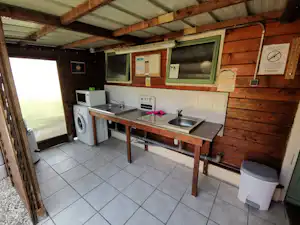 Holzhaus mit Küchenzeile: Spüle, Arbeitsplatte, Kühlschrank und Waschmaschine, Fliesenboden und Schrankwände an der Wand.