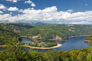 Blick auf einen Fluss und Stausee im grünen Tal mit Uferwegen, kleinen Siedlungen und bewaldeten Hügeln.