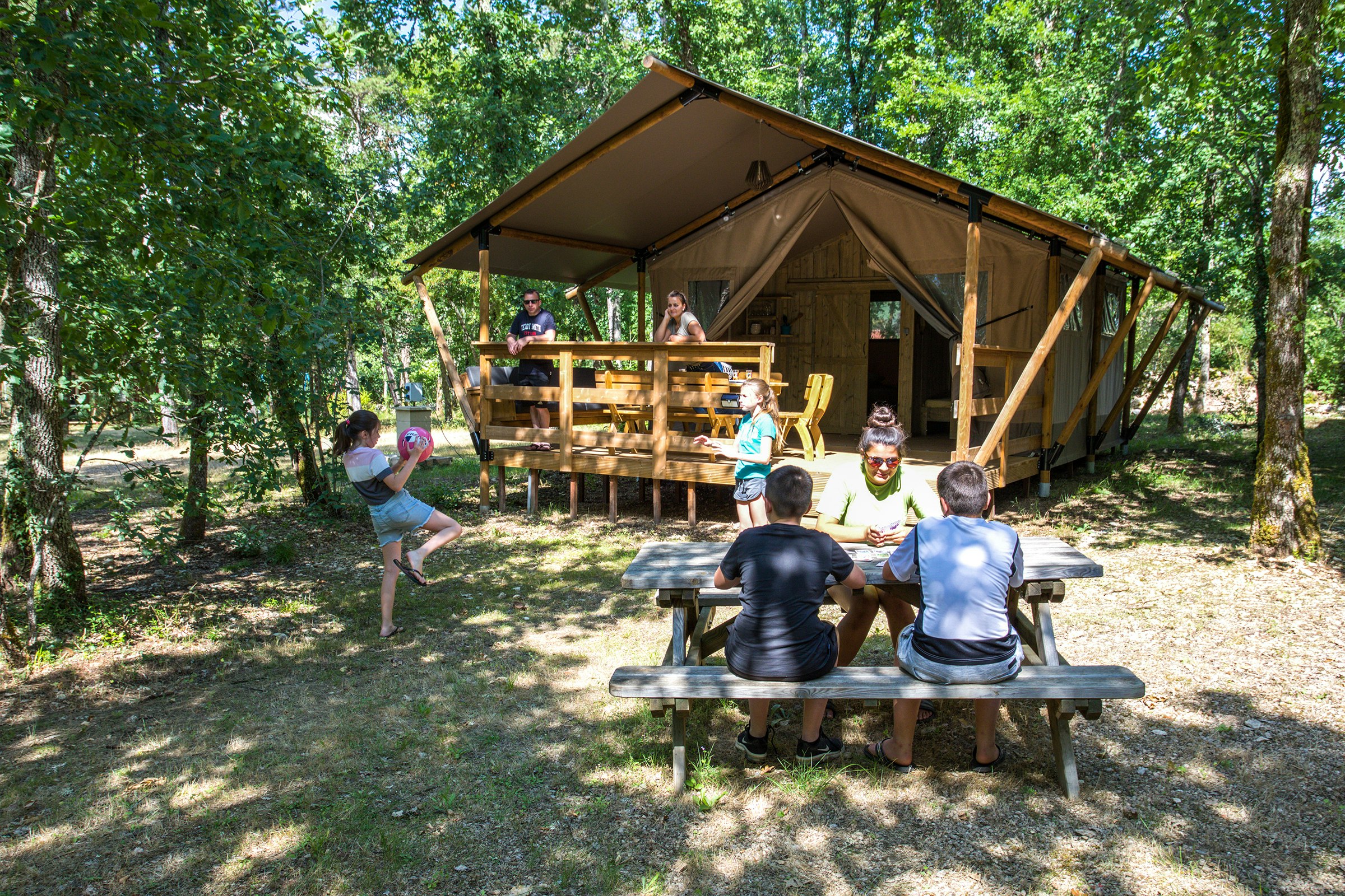 Camping La Peyrugue - Glamping-Zelt mit Terrasse umgeben von Bäumen