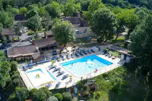 Luftaufnahme eines Campingplatzes mit großem Pool, Liegen und mehreren Gebäuden, umgeben von vielen Bäumen.