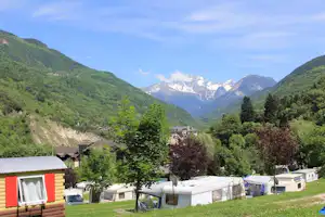 Campingplatz mit Wohnwagen und Zelten auf einer Wiese, im Hintergrund Berge und bewaldete Hänge.