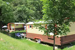 Zwei Wohnwagen auf einem Campingplatz im Grünen, mit Rasenfläche, Gartenstühlen und Bäumen im Vordergrund.
