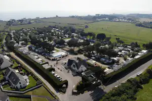 Luftaufnahme eines Campingplatzes mit Stellplätzen, Wohnwagen und Gebäuden, umgeben von grünen Wiesen und Bäumen.