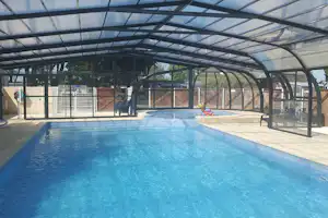 Blauer Campingpool unter einem transparenten Dach, mit Liegen und Absperrgitter im Hintergrund.