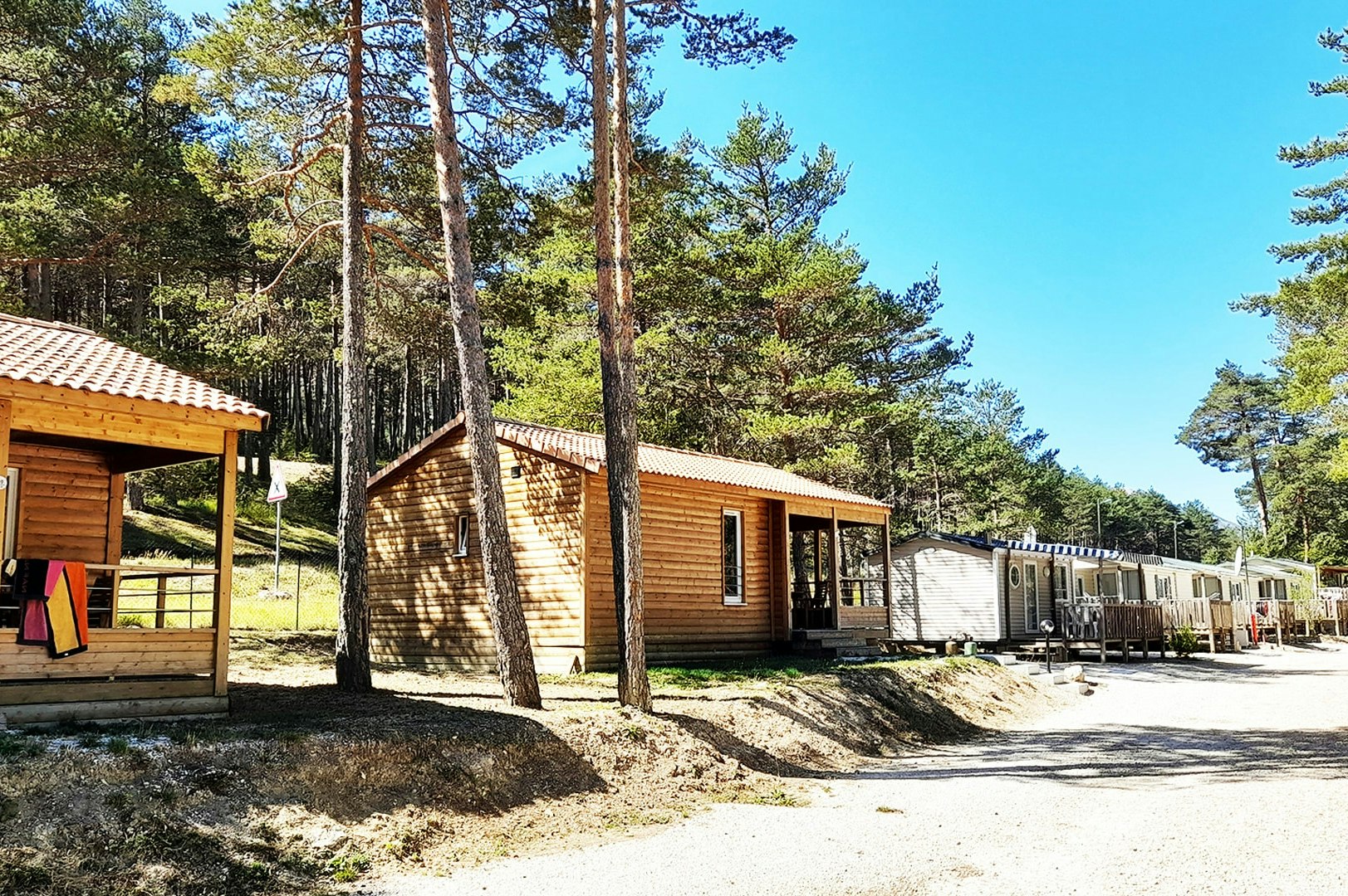 Holzhütten auf einem Campingplatz, mit Wegen, Holzterrassen und Bäumen im Hintergrund.