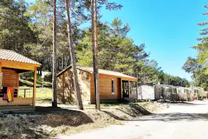 Holzhütten auf einem Campingplatz, mit Wegen, Holzterrassen und Bäumen im Hintergrund.