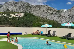 Camping-Pool mit Liegen und Sonnenschirmen, Kinder im Wasser, im Hintergrund Berge und Felswände.