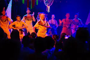 Tanzgruppe auf der Bühne bei einem Camping-Festival, farbige Lichter und bunte Dekoration im Hintergrund.