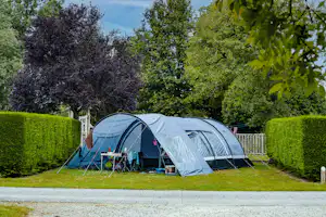 Zelt im Campingplatz mit zwei Eingängen, davor Gartenmöbel und ein kleiner Tisch, umgeben von Hecken und Bäumen.