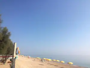 Sandstrand mit gelben Sonnenschirmen, Promenade und Blick aufs ruhige Meer unter klarem Himmel.