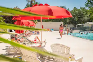 Roter Sonnenschirm am Pool mit Liegestühlen, im Hintergrund Kinder im Wasser und weitere Schirme auf der Terrasse.