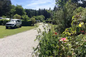 Einfahrt auf dem Campingplatz mit Kiesweg, weißem Geländewagen und gepflegtem Grün mit Büschen und Bäumen.