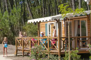 Holz-Mobilheim mit Veranda und Markise im Wald, Kinder und Erwachsene vor der Tür auf dem Holzgeländer.