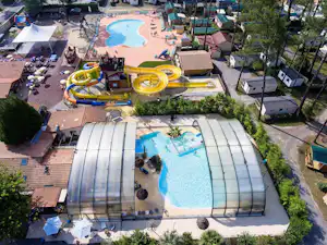 Luftaufnahme von zwei Pools und gelben Wasserrutschen auf dem Campingplatz, mit Sonnenschirmen, Gebäuden und Wegen.