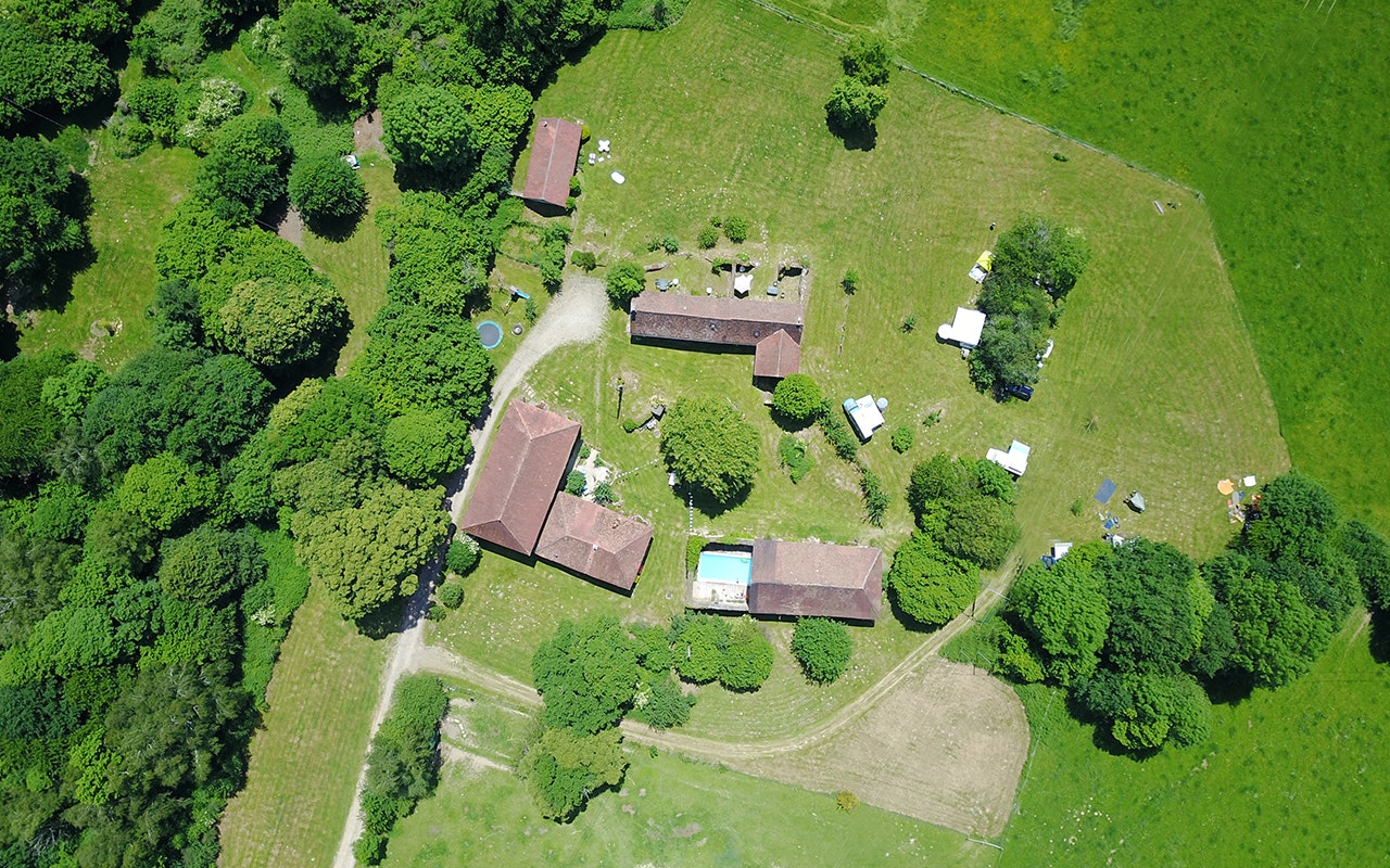 Luftaufnahme einer Campinganlage mit mehreren Gebäuden, Stellplätzen, Wegen, Bäumen und einem kleinen Pool im grünen Gelände.