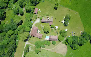 Luftaufnahme einer Campinganlage mit mehreren Gebäuden, Stellplätzen, Wegen, Bäumen und einem kleinen Pool im grünen Gelände.