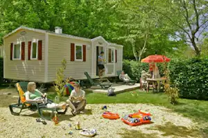 Wohnwagen mit Terrasse und Markise, daneben Campingstühle und Spielzeug auf dem Stellplatz im Grünen.