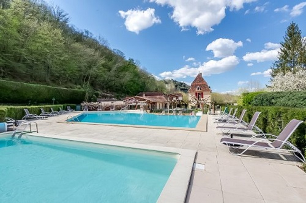 Camping-Pool mit Liegen auf der Terrasse, im Hintergrund ein Gebäude und Bäume am Hang.