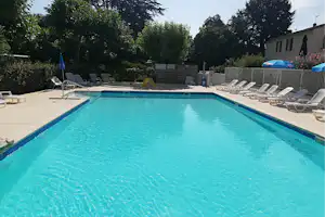 Schwimmbecken mit blauem Rand, Liegestühlen auf der Terrasse und Sichtschutzzaun, im Hintergrund Bäume und ein Gebäude.