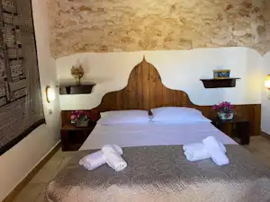 Bett in einem Campingzimmer mit weißen Kissen, Holz-Kopfteil, Nachttischen und Wand aus Naturstein.