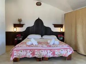 Schlafzimmer im Campingbereich mit Doppelbett, dekorativer Bettwäsche, zwei Nachttischen und warmen Lampen an den Wänden.