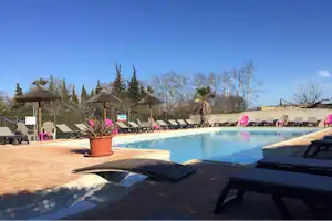 Schwimmbecken auf dem Campingplatz mit Sonnenliegen, Sonnenschirmen und Terrassenboden, im Hintergrund weitere Liegen und Bäume.