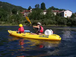Gelbes Schlauchboot auf dem Fluss, zwei Personen mit Schwimmwesten, im Hintergrund Bäume und Campinghäuser.