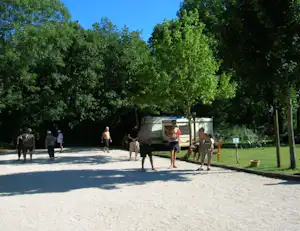 Campingplatz-Weg zwischen Bäumen, im Hintergrund ein Wohnwagen und mehrere Personen auf dem Kiesweg.