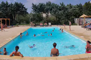 Blauer Camping-Pool mit mehreren Schwimmern, Liegen am Beckenrand, Sonnenschirm und Bäumen im Hintergrund.