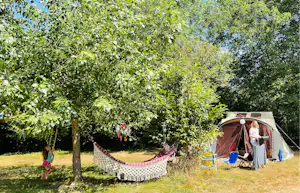 Campingzelt im grünen Garten, Hängematte zwischen Bäumen und Sitzbereich mit Stühlen und Tisch.