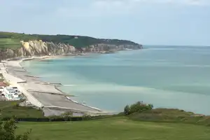 Blick auf einen Campingplatz an der Küste mit Zeltdach-Zelten, Wiese und Meer vor den Klippen.