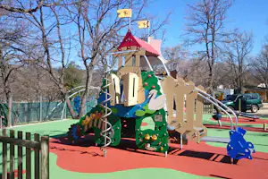 Bunter Kletterturm auf dem Spielplatz im Campingpark, mit Rutsche, Geländer und Spielgeräten vor Bäumen.
