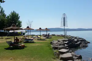 Camping La Spiaggia - Stellplatz und Liegewiese mit Sonnenschirmen und Liegestühlen am Trasimenischer See