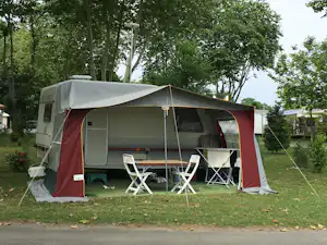 Campingzelt mit Vorzelt und Sitzgruppe auf einem Stellplatz im Grünen, umgeben von Bäumen und Rasen.