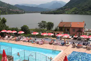 Camping La Tartufaia - Poolanlage mit Liegestühlen und Sonnenschirmen und der Lago di Endine im Hintergrund