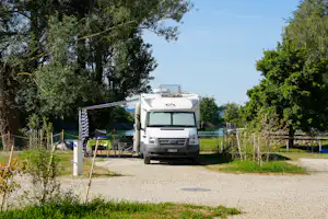 Wohnmobil auf einem Campingplatz-Stellplatz, mit Markise und Vorzelt, umgeben von Bäumen und Hecken.