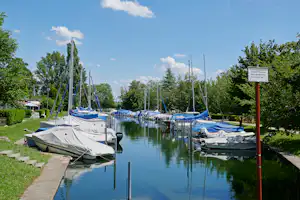 Bootssteg am See mit mehreren Segelbooten, daneben Zelte und Rasenfläche am Campingplatz.