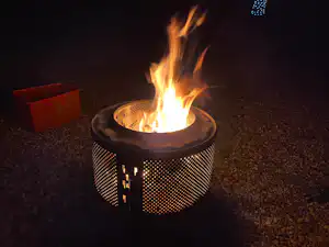 Lagerfeuer in einem Feuerkorb mit Flammen auf einem Kiesboden, im Hintergrund eine dunkle Umgebung.