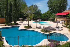 Camping-Pool mit Sonnenschirmen, Liegestühlen und zweitem Becken auf der Terrasse, umgeben von Bäumen und Hecken.